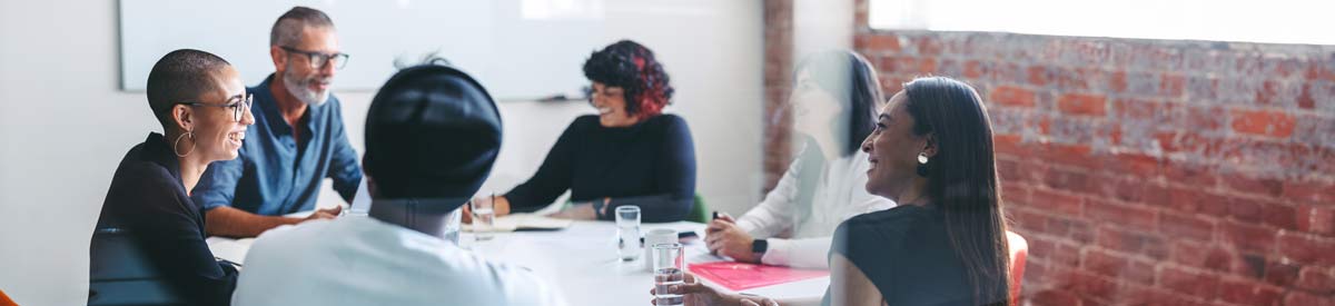 Employees in a meeting at a table in a well lit room, the employees are smiling and sharing information