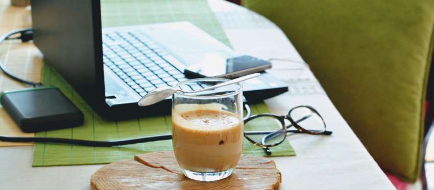 A computer next to a cup of coffee