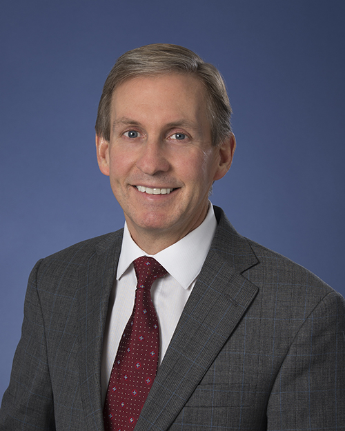 Peter Pisters smiles in a grey suit with burgundy tie.