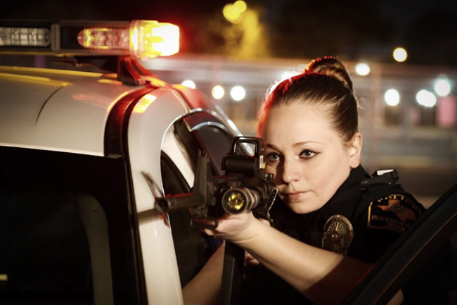 Office Lincoln aims a rifle from behind the the open door of a police car